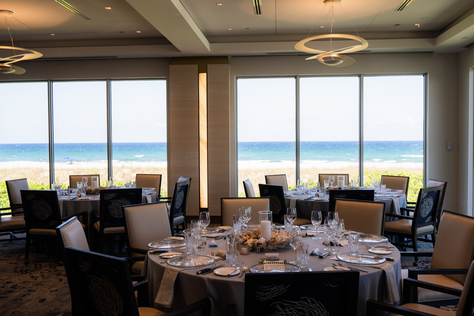Elegant reception room at the Delray Beach Club, round tables set for dinner with floor-to-ceiling windows and ocean views